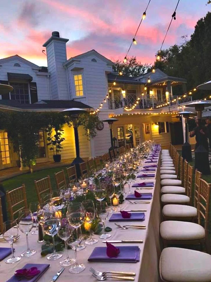 A long table laid for dinner at dusk, under string lights